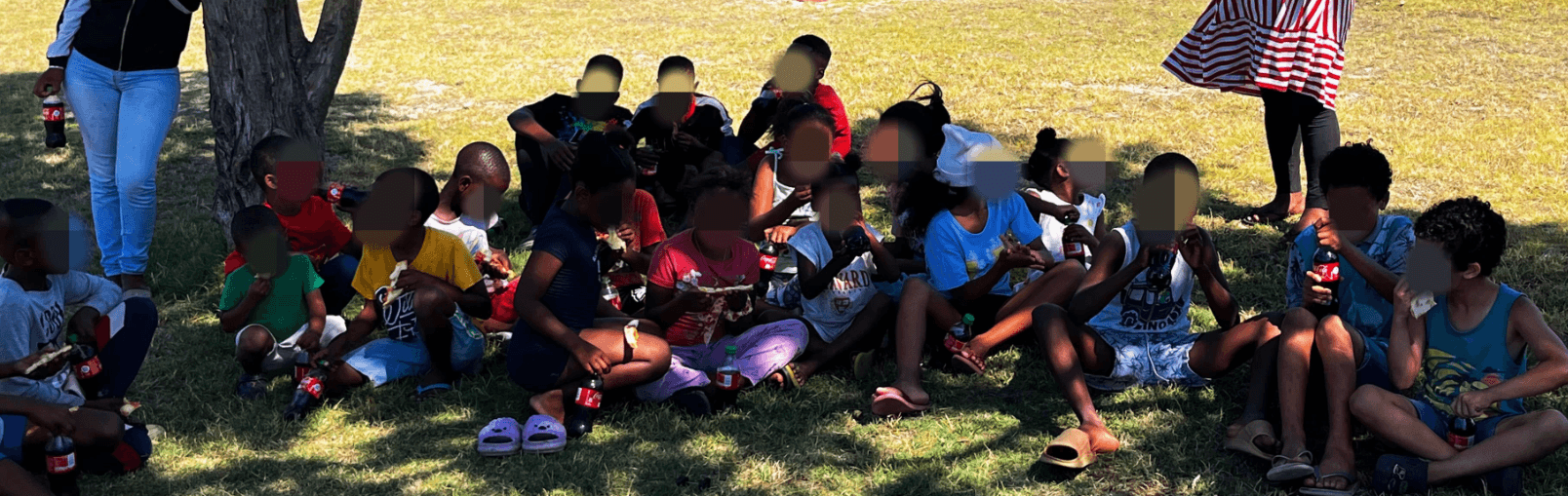 Children sharing a meal together outdoors in the shade.