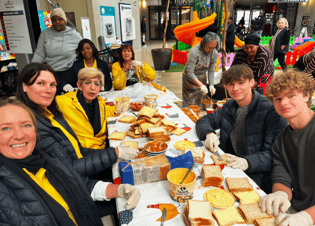 Volunteers and supporters preparing meals around a long table.